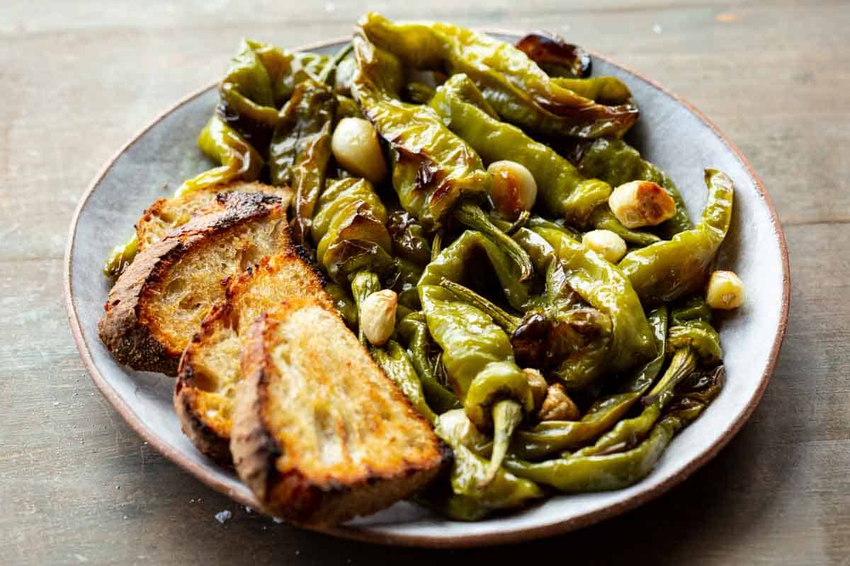 A round plate of roasted garlic and long hot peppers with toasted bread.
