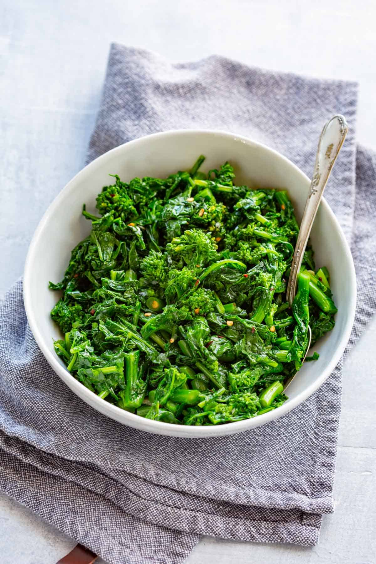 A white bowl of sautéed rapini on a gray cloth.