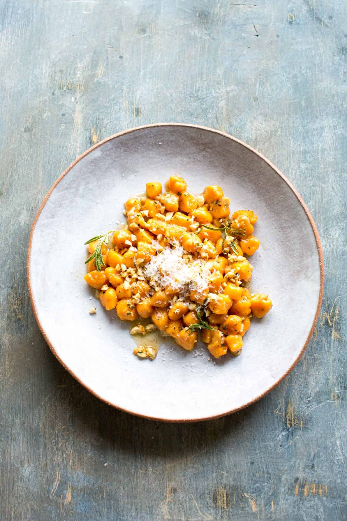 Plate of homemade sweet potato gnocchi topped with rosemary and parmesan.