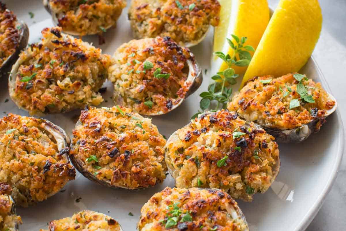 Stuffed clam dish served on a white plate with lemon wedge garnish.