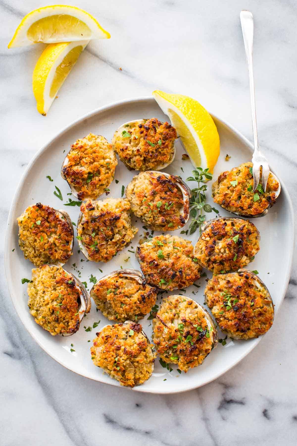 Seafood dish served on a plate with a small oyster fork stuck into a stuffed clam.
