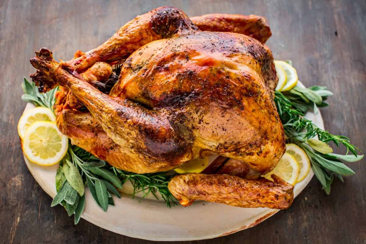 An Italian style roasted whole turkey on a platter with fresh herbs and lemon slices.