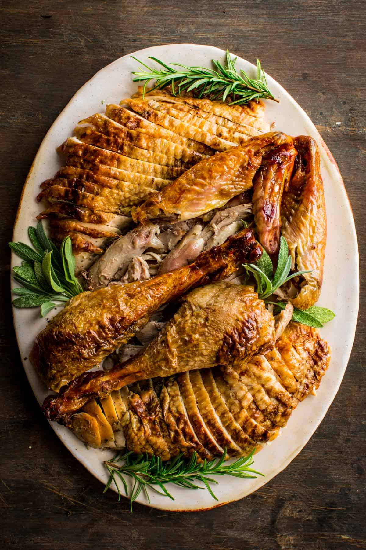 Beautifully carved turkey on a platter garnished with fresh herbs.