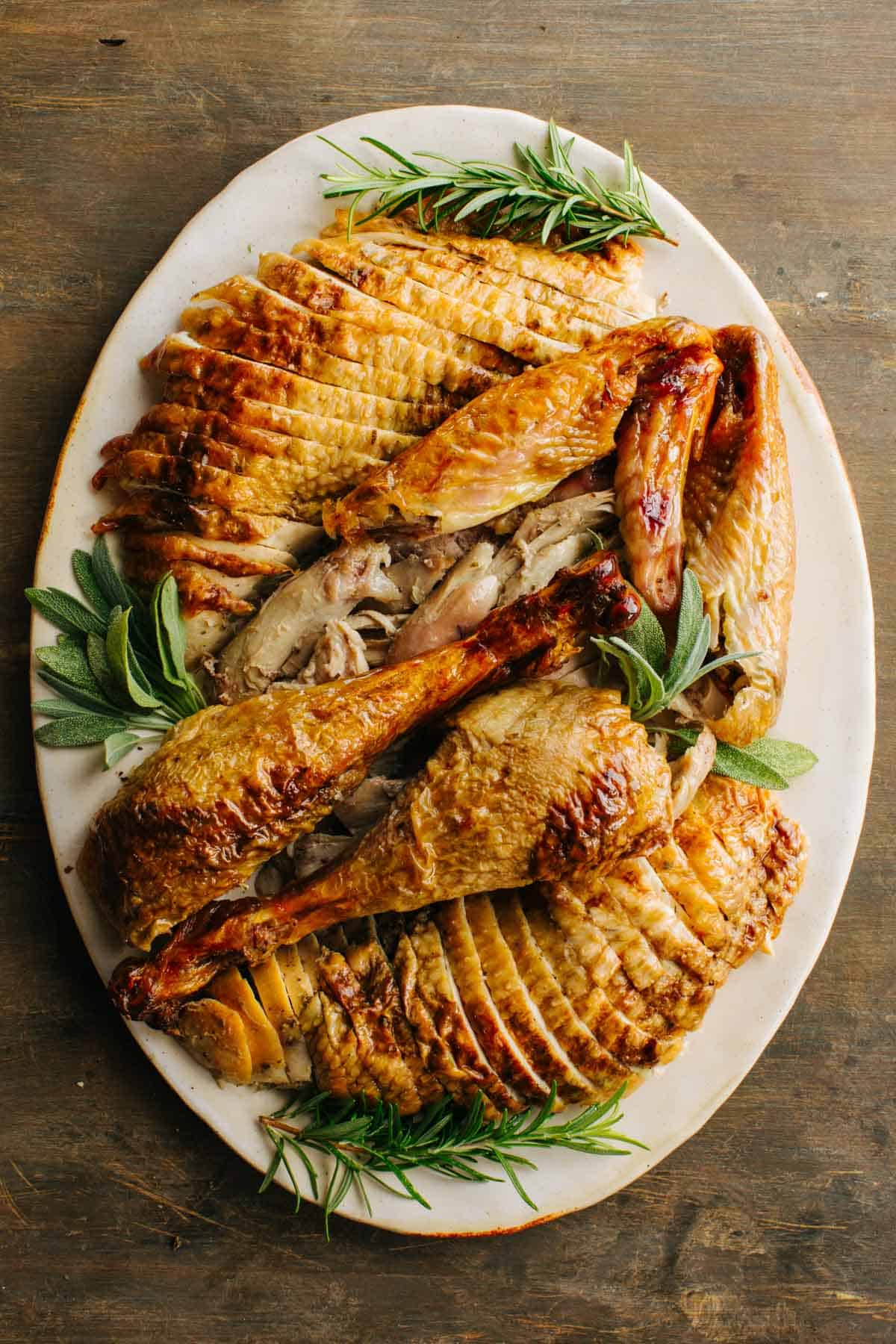 Sliced turkey on a white platter with sprigs of fresh herbs.
