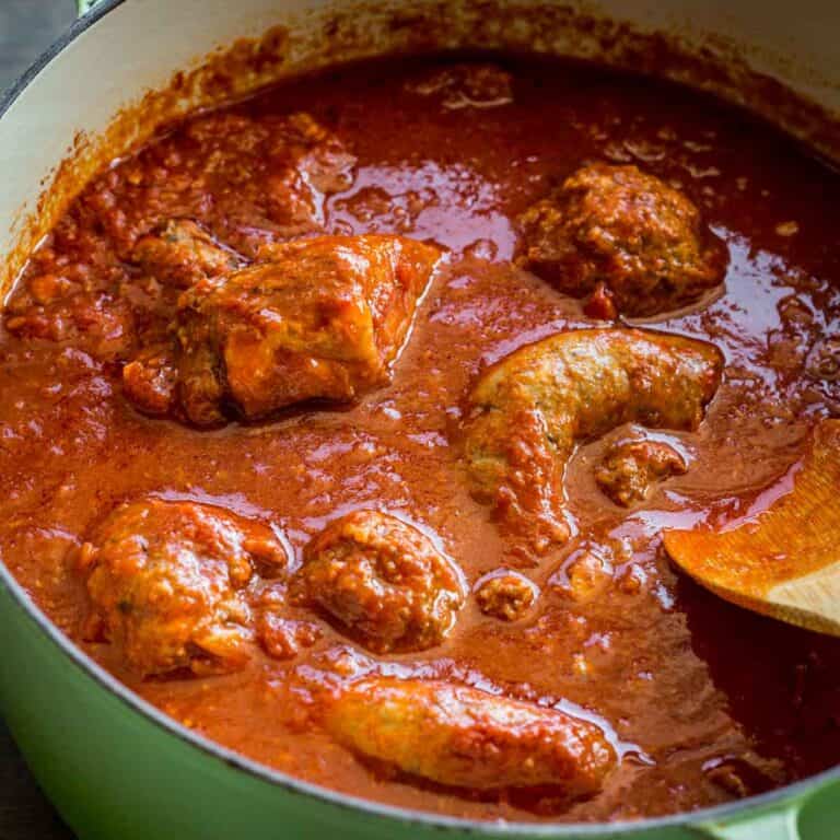 A pot of assorted meats cooking in red sauce.