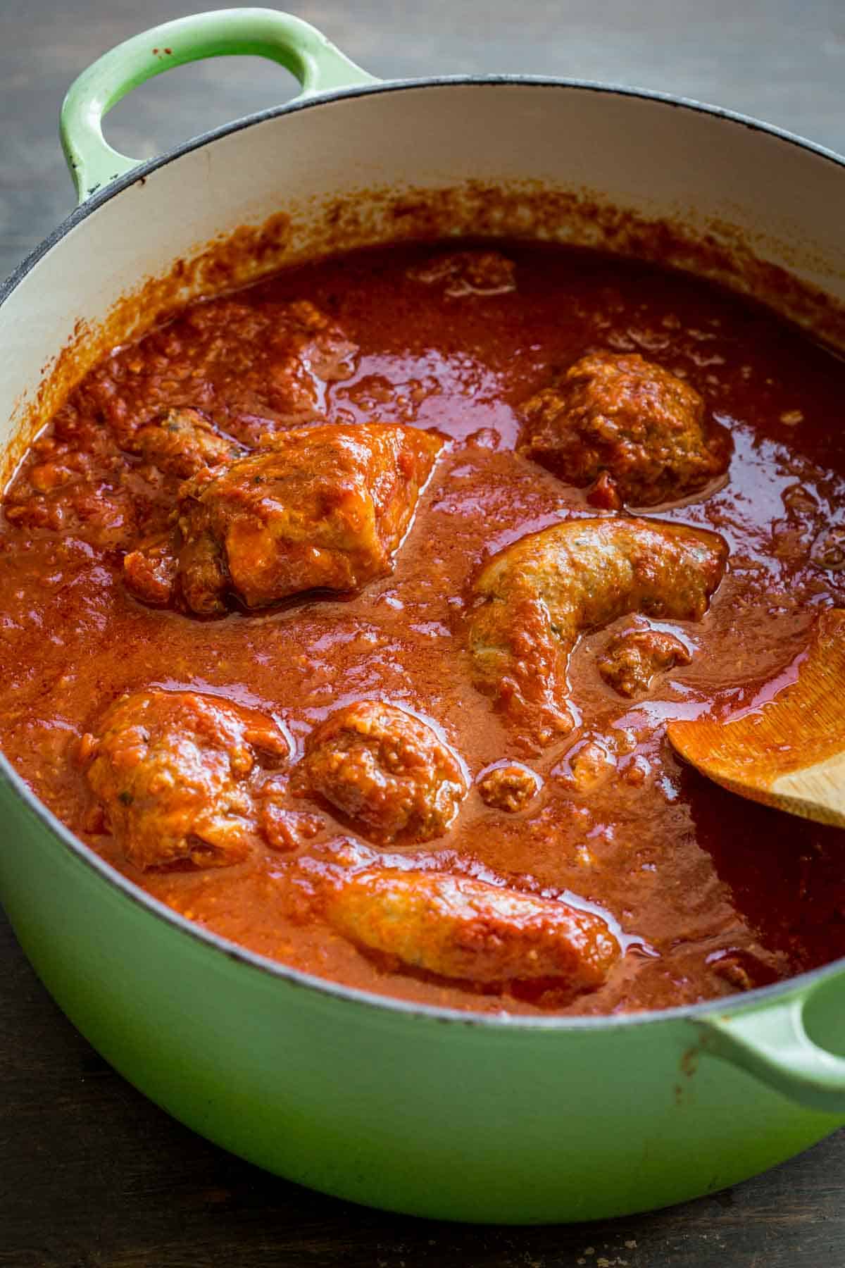 A large Dutch oven filled with Italian red sauce and various meats.