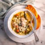 serving Italian meatball wedding soup in a white bowl with a spoon and bread.