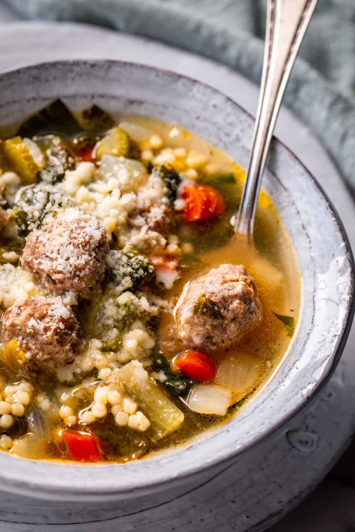 A bowl of Italian wedding soup with a spoon inside.
