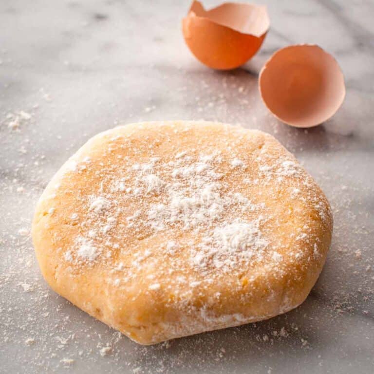 A disc of pasta frolla dough dusted with flour on top and egg shells in the background.