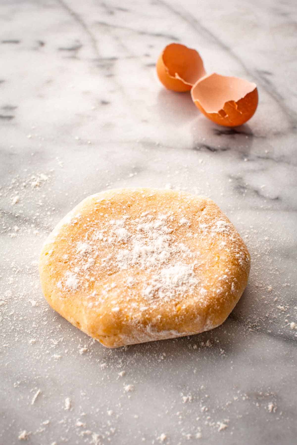 A disc of pastry dough with egg shells in the back ground.