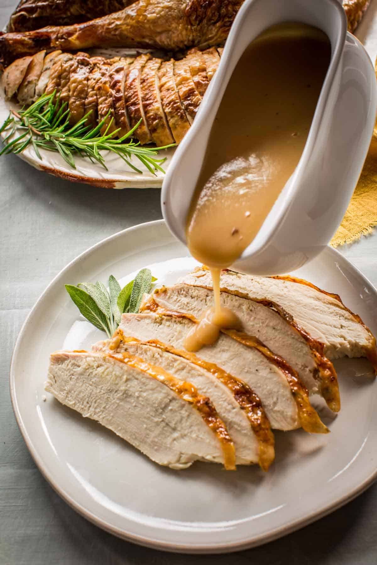 A gravy boat pouring gravy on sliced turkey breast.