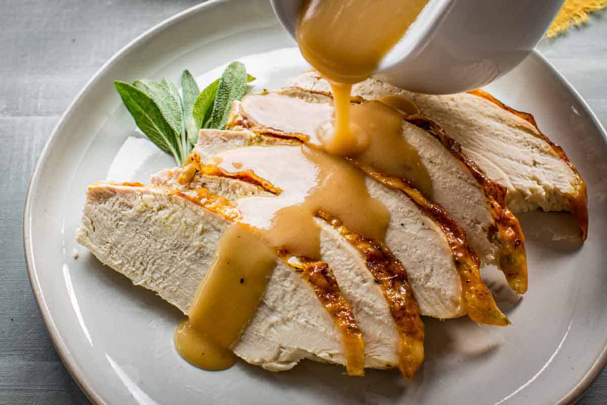 A gravy boat pouring gravy over a plate of turkey.