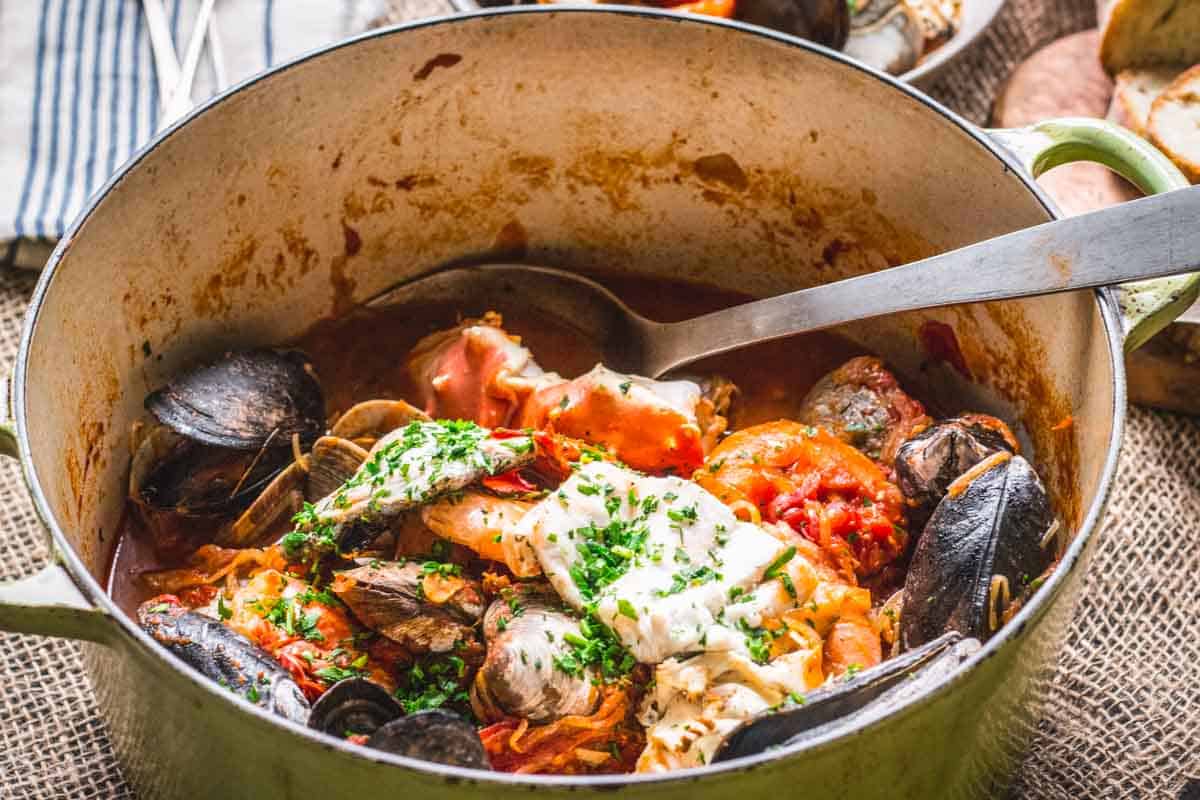 A large spoon in a pot of seafood stew.