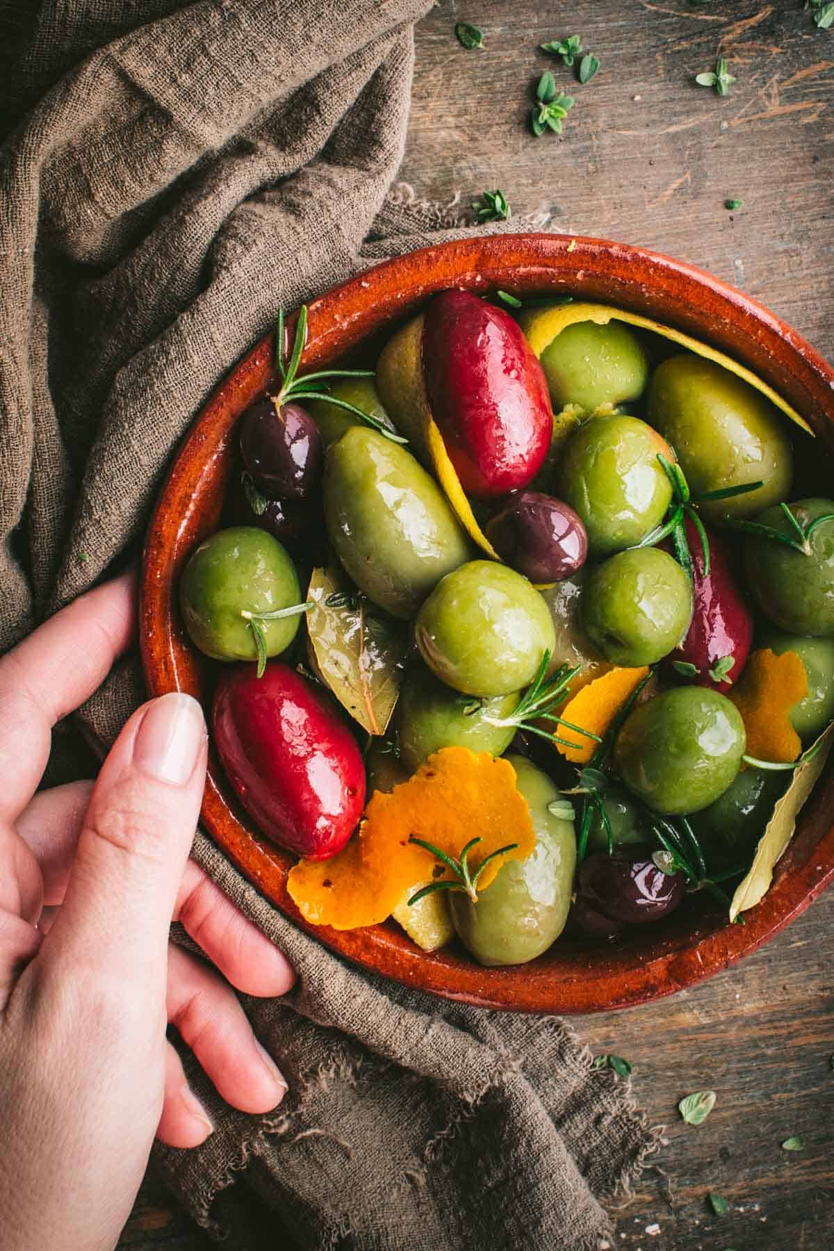 A hand holding a dish of olives over an olive green napkin.