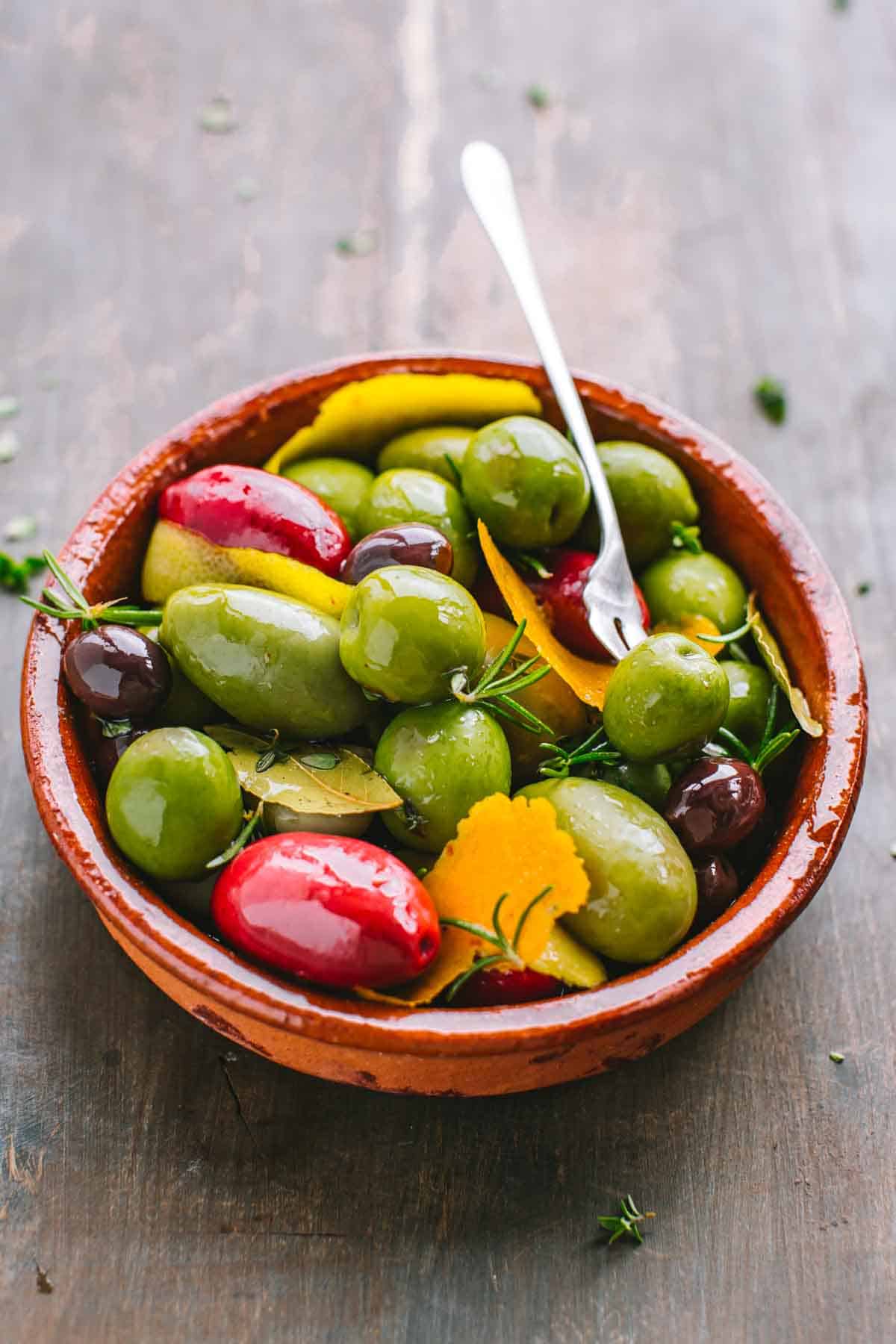 A dish of olives with one speared with a cocktail fork.