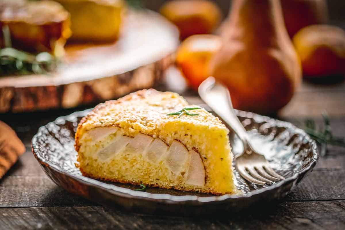 The side of a slice of ricotta cake on a plate with pears studded throughout.