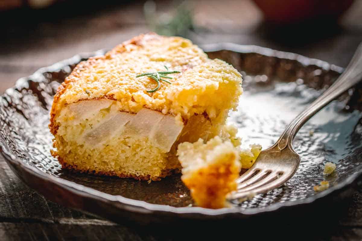 A half-eaten wedge of Italian ricotta cake with pears on a small plate next to a fork.