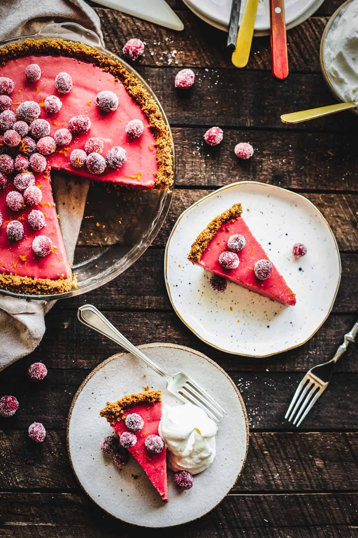 Cranberry Pie with 2 slices taken out, on plates with forks with whipped cream and sugared cranberries