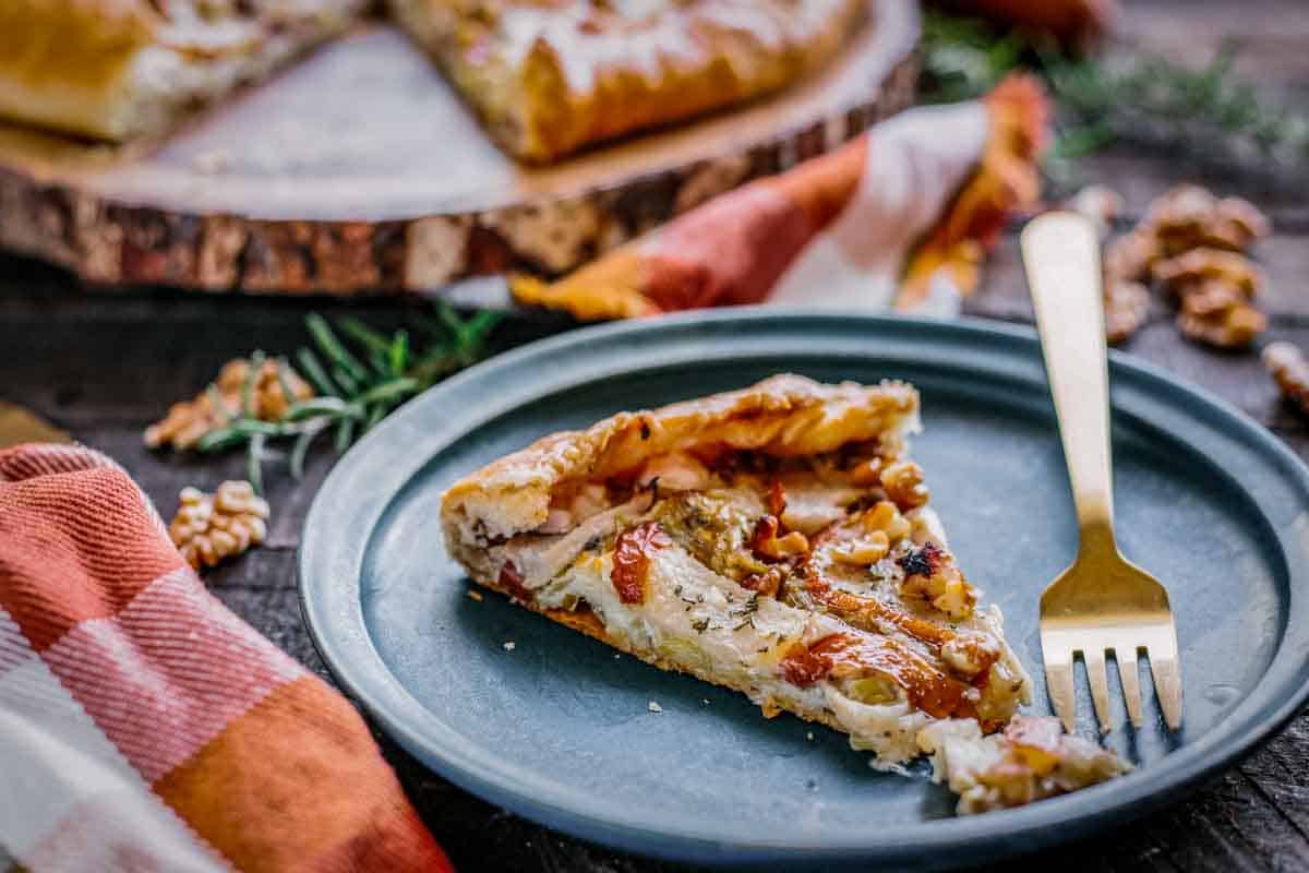 A gold fork taking a bite out of a pear galette on a blue plate.