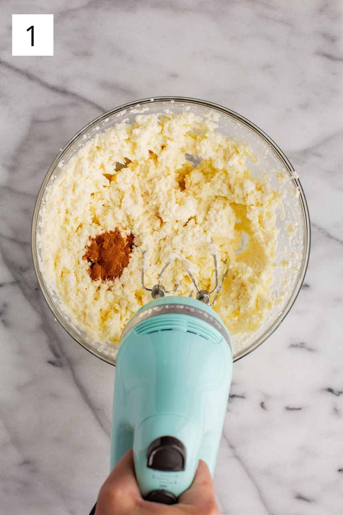 An electric mixer mixing cinnamon into ricotta.
