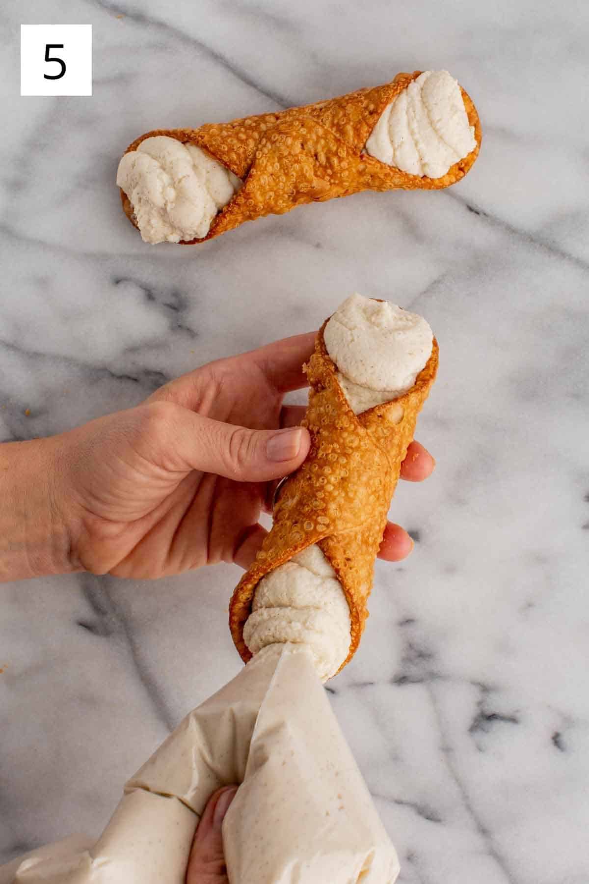 Piping cannoli cream into a cannoli shell.