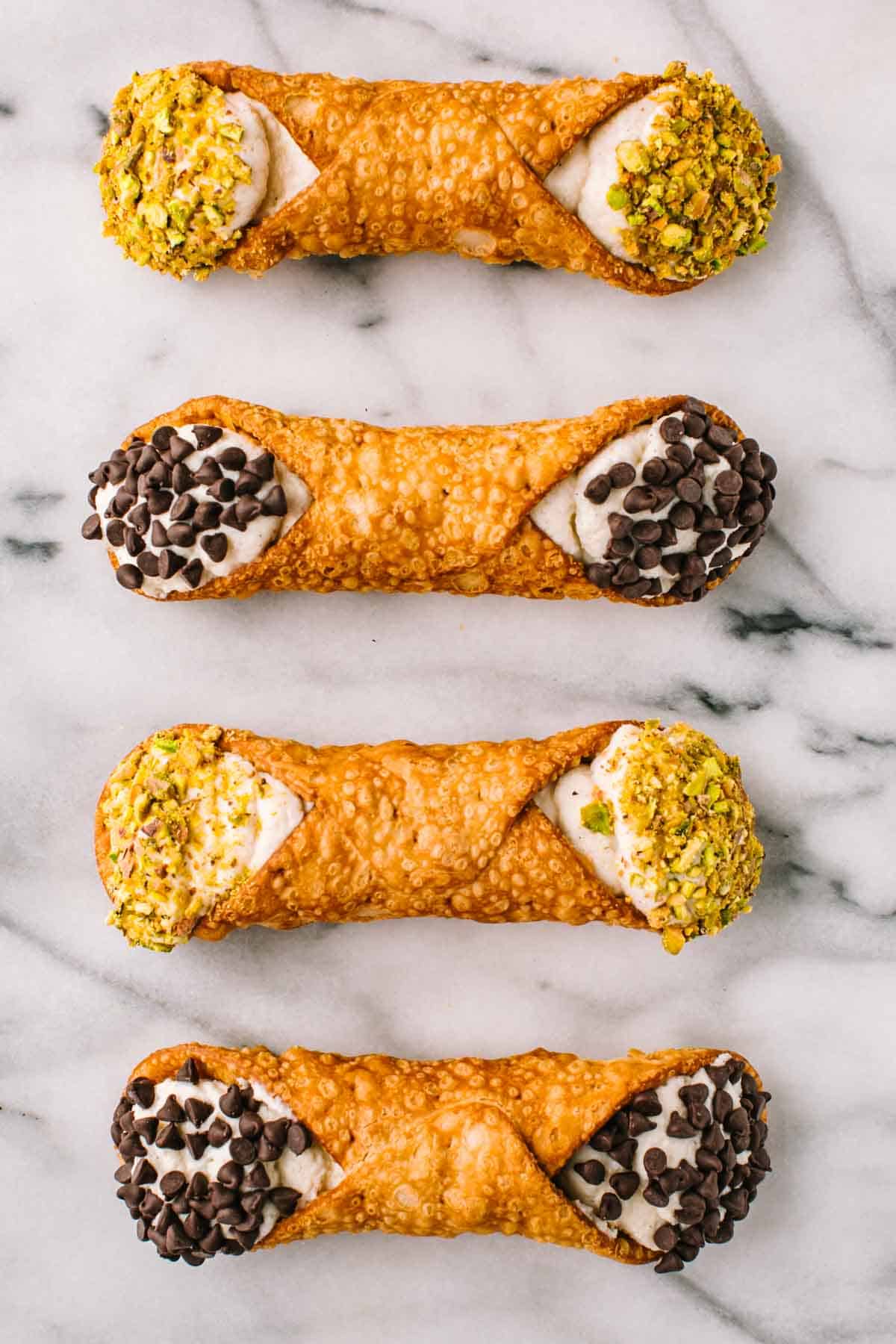 Four cannoli in a row on a marble board.