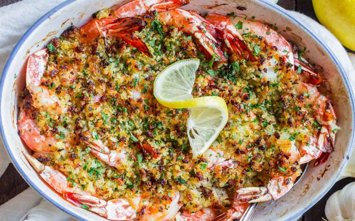 A baking dish with shrimp scampi, breadcrumbs, and lemon on top.