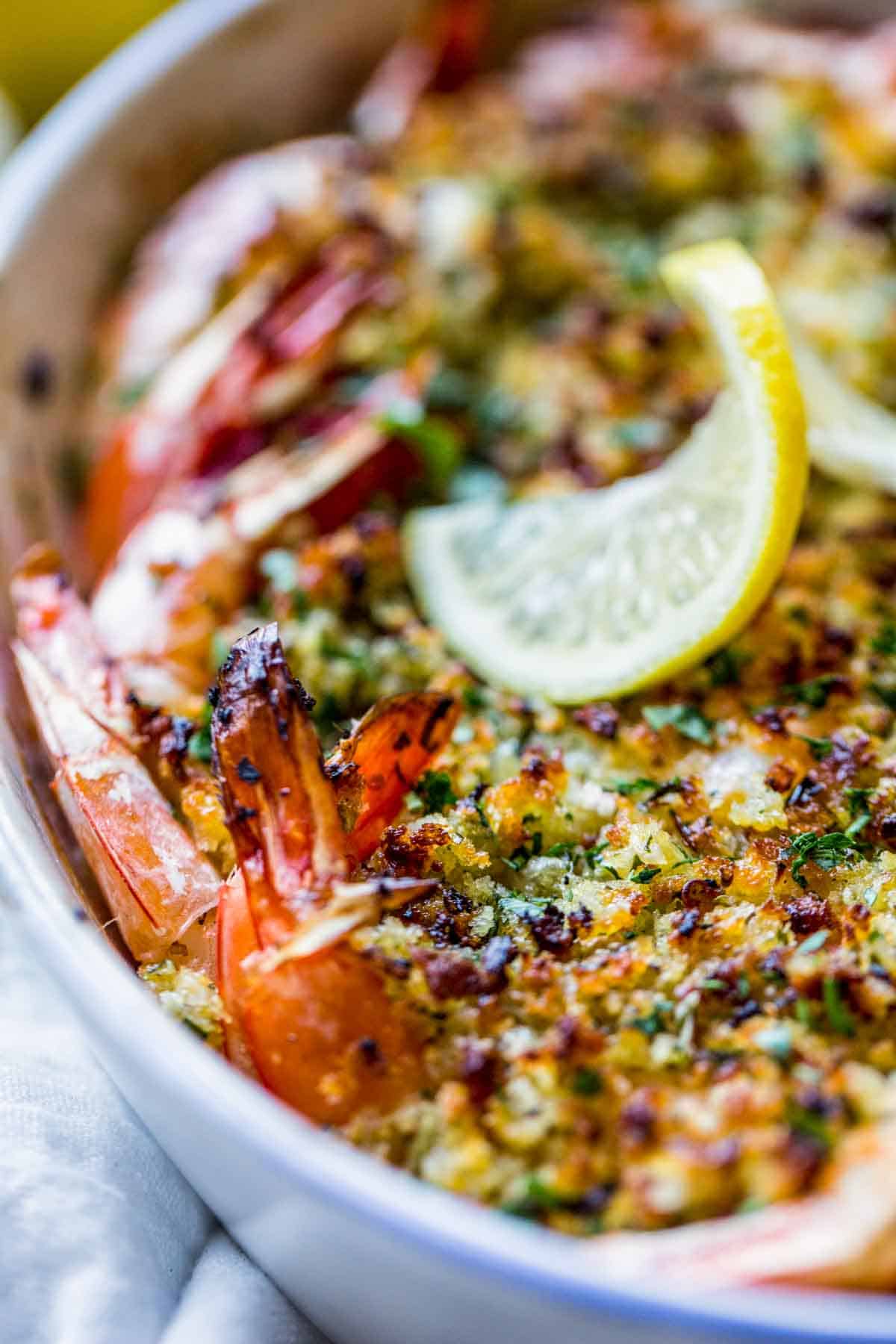 Close up of shrimp tails and breadcrumbs on baked shrimp scampi with a lemon twist in the background.