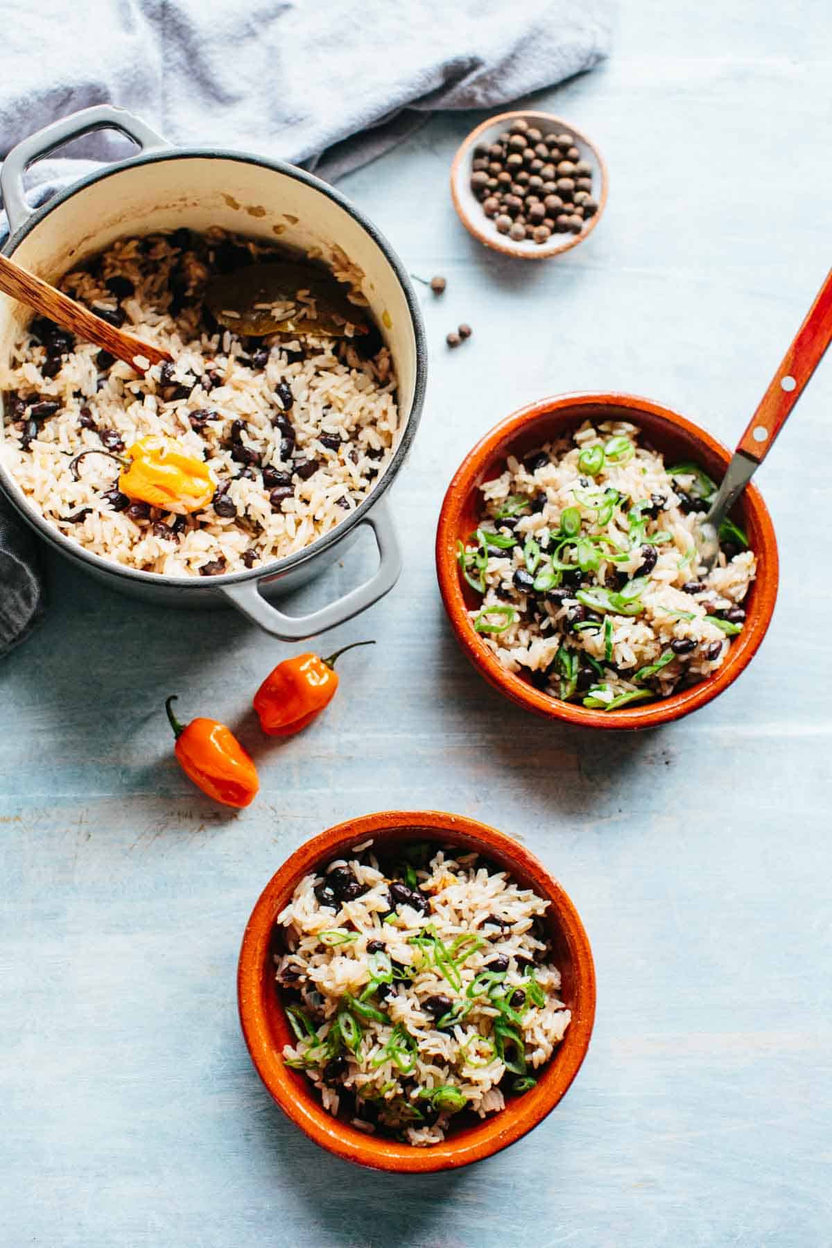 A tables cape with a pot and bowls of Caribbean rice and beans with scallions and scotch bonnet chillies.