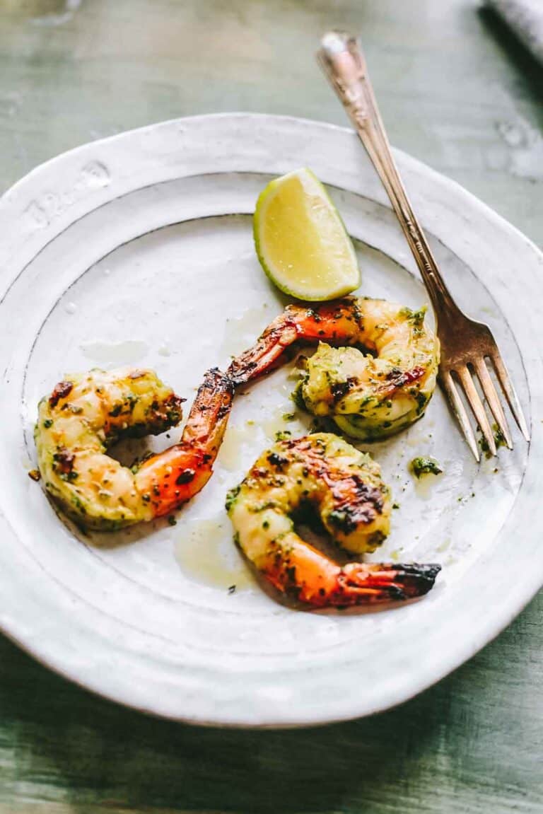 Three marinated grilled shrimp with a lime and a fork.