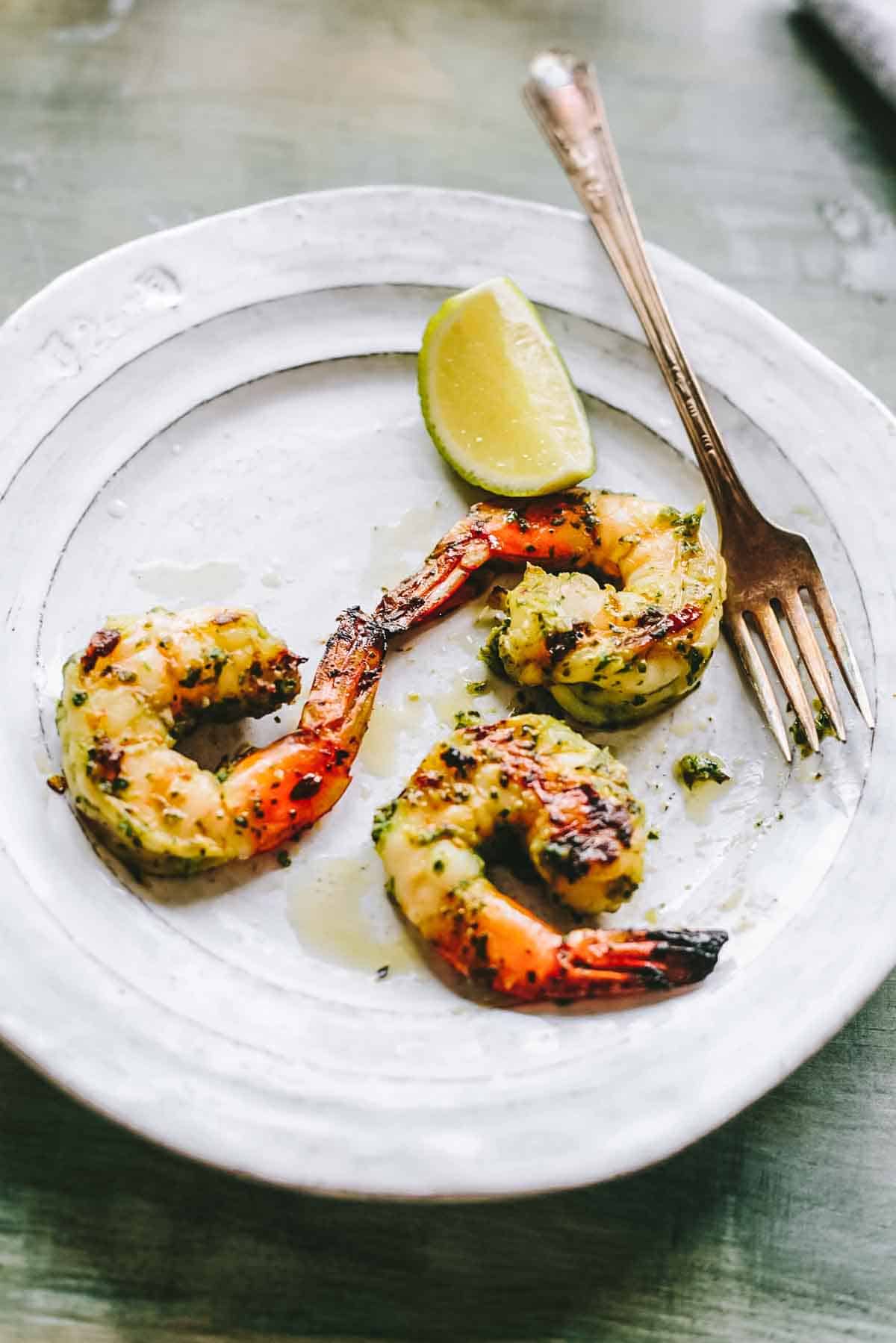 Three marinated grilled shrimp with a lime and a fork.