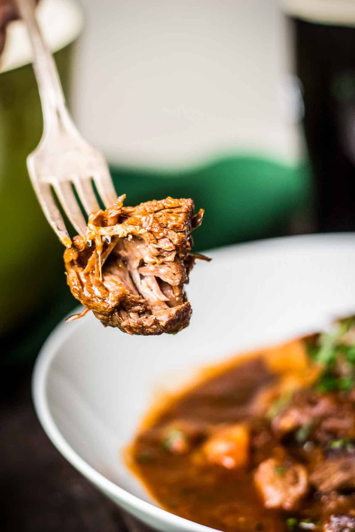 Close up of cooked beef stew meat on a fork over a bowl of Irish stew.