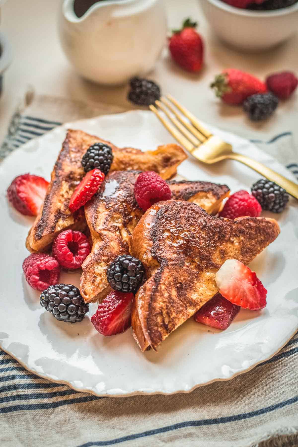 Three pieces of French toast on a plate with fresh berries.