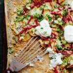 A spatula scooping up cheesy potatoes on a parchment-lined baking sheet.