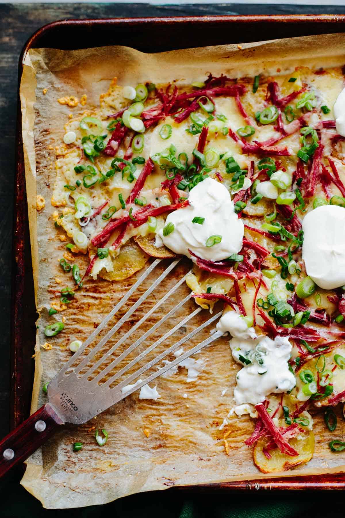 A spatula scooping up cheesy potatoes on a parchment-lined baking sheet.