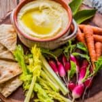 A small stone bowl of skordalia among fresh veggies and pita points.