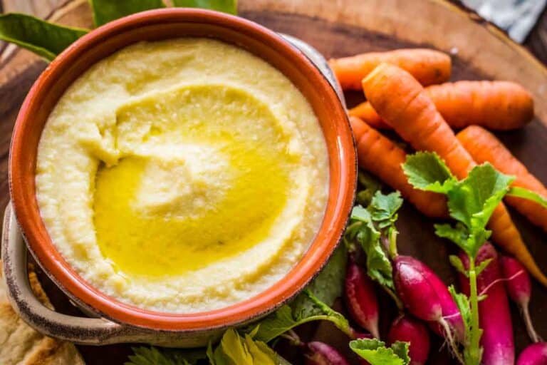 A bowl of Greek garlic and potato dip with carrots and radishes.