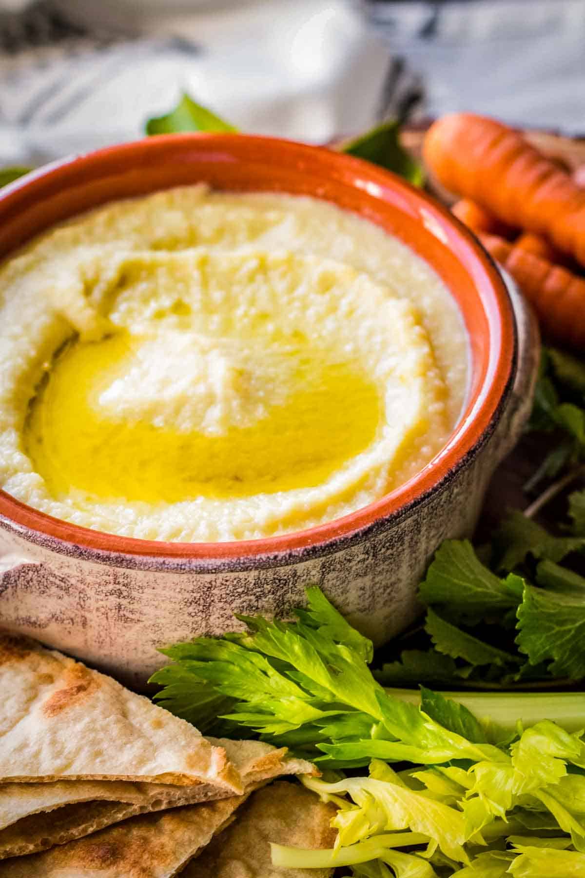 A pool of olive oil on a bowl of skordalia dip with fresh veggies on a tray.