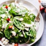 A hand scooping up some spinach leaves with goat cheese, pancetta and red onions with a fork.