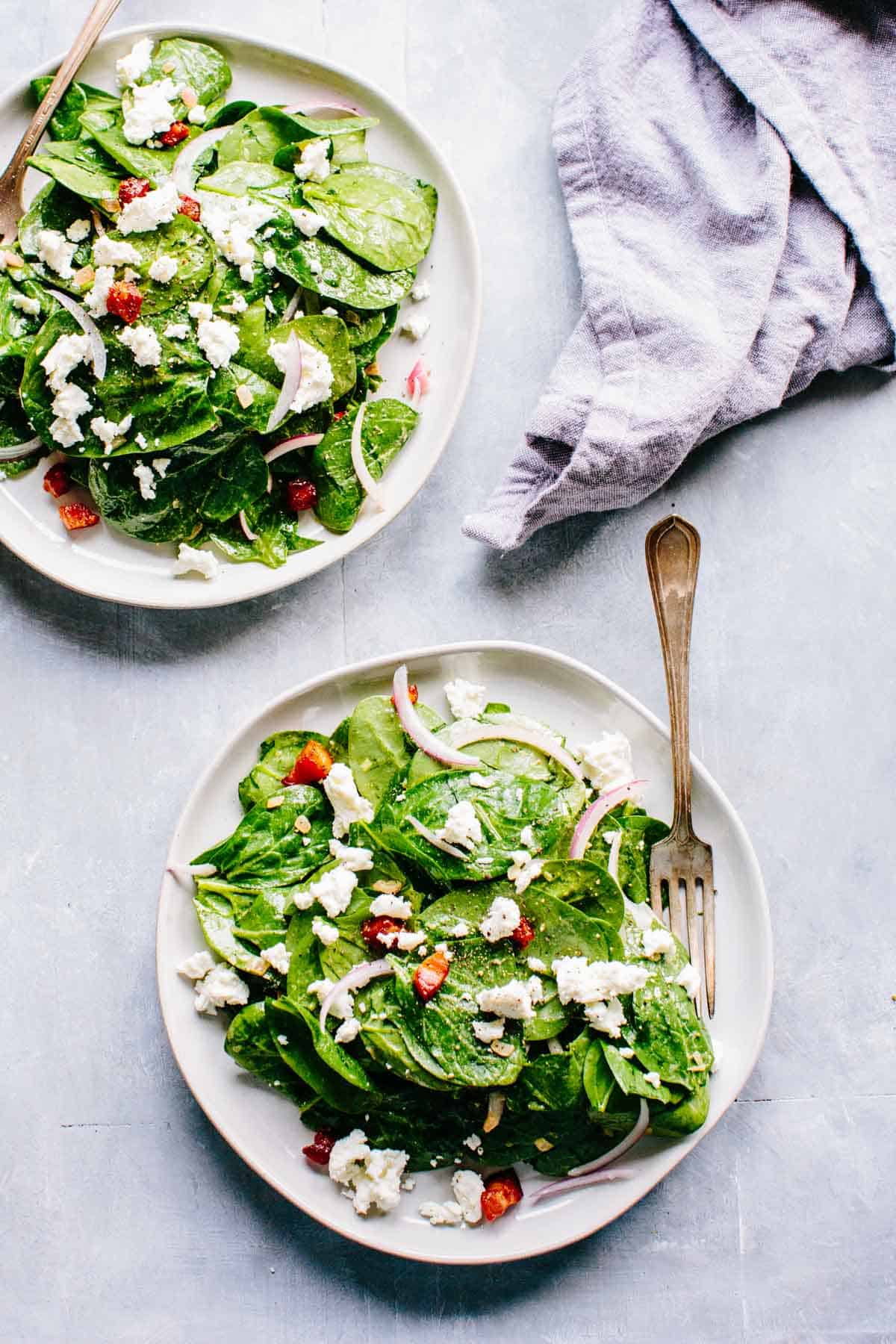 Two plates of warm spinach salad with goat cheese, pancetta and red onions.