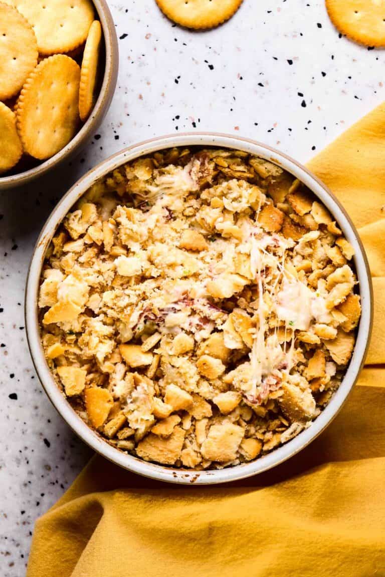 A baked dish of warm cheesy bacon dip with ritz crackers.