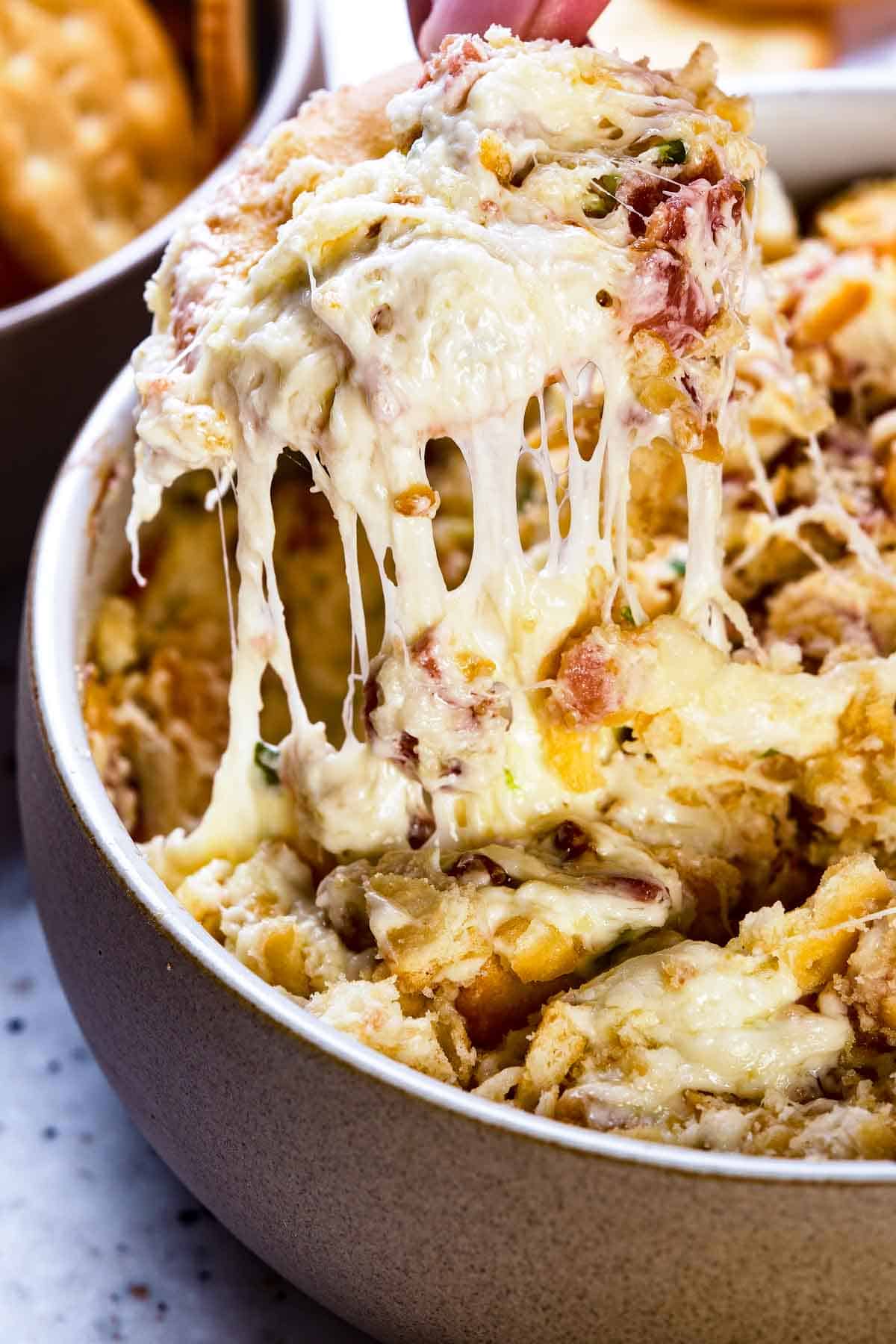 Melted cheese dripping off a scoop of dip on a cracker.
