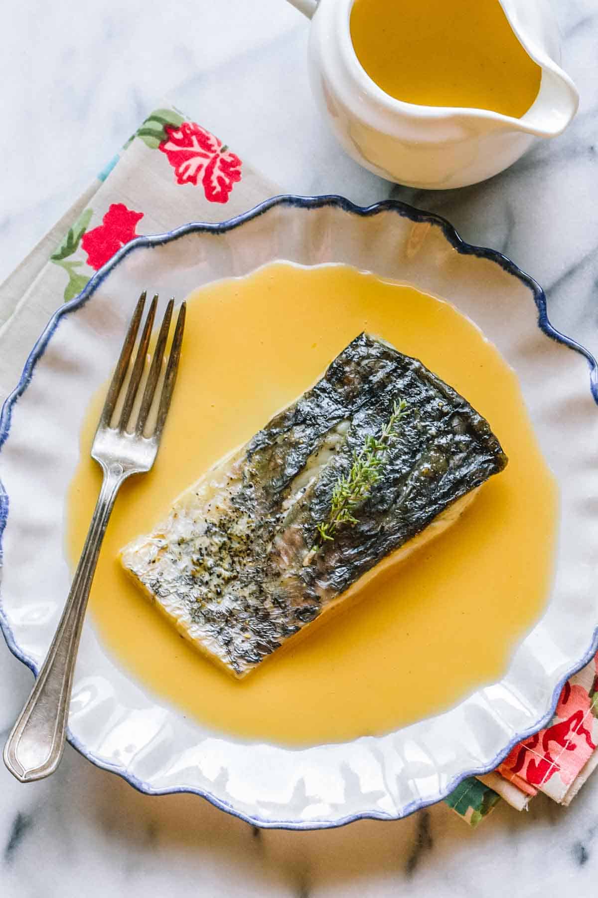 A piece of fish on top of beurre blanc sauce with a fork. 