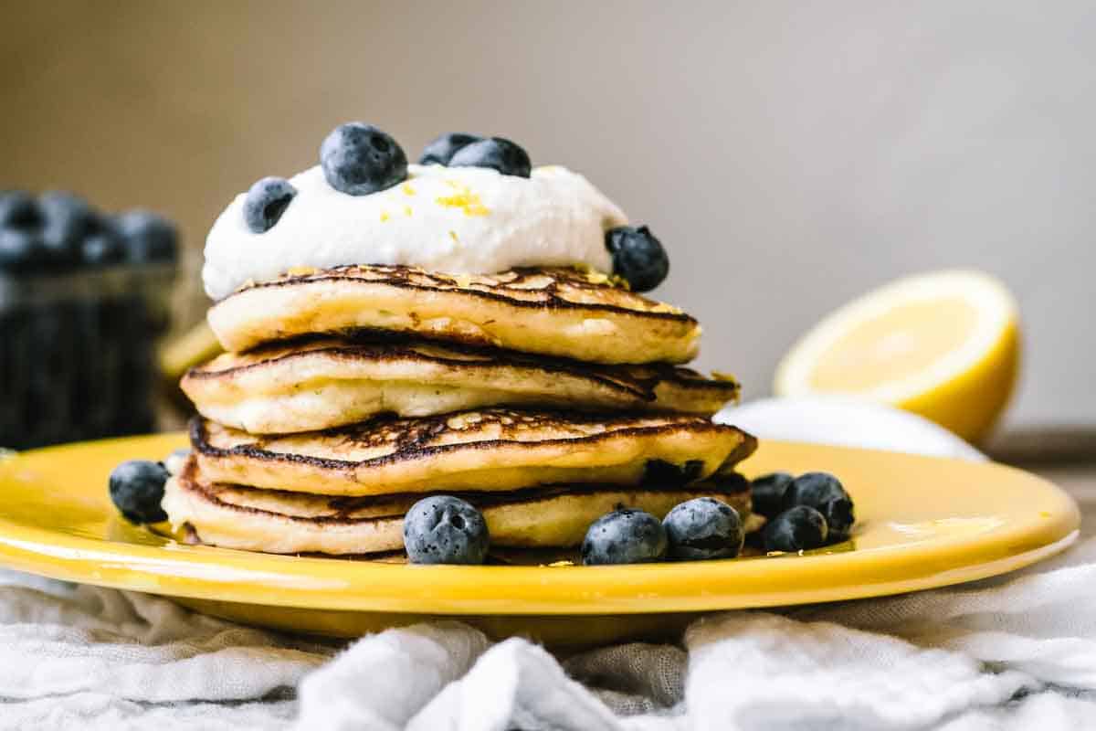 A big stack of lemon ricotta pancakes with blueberries.