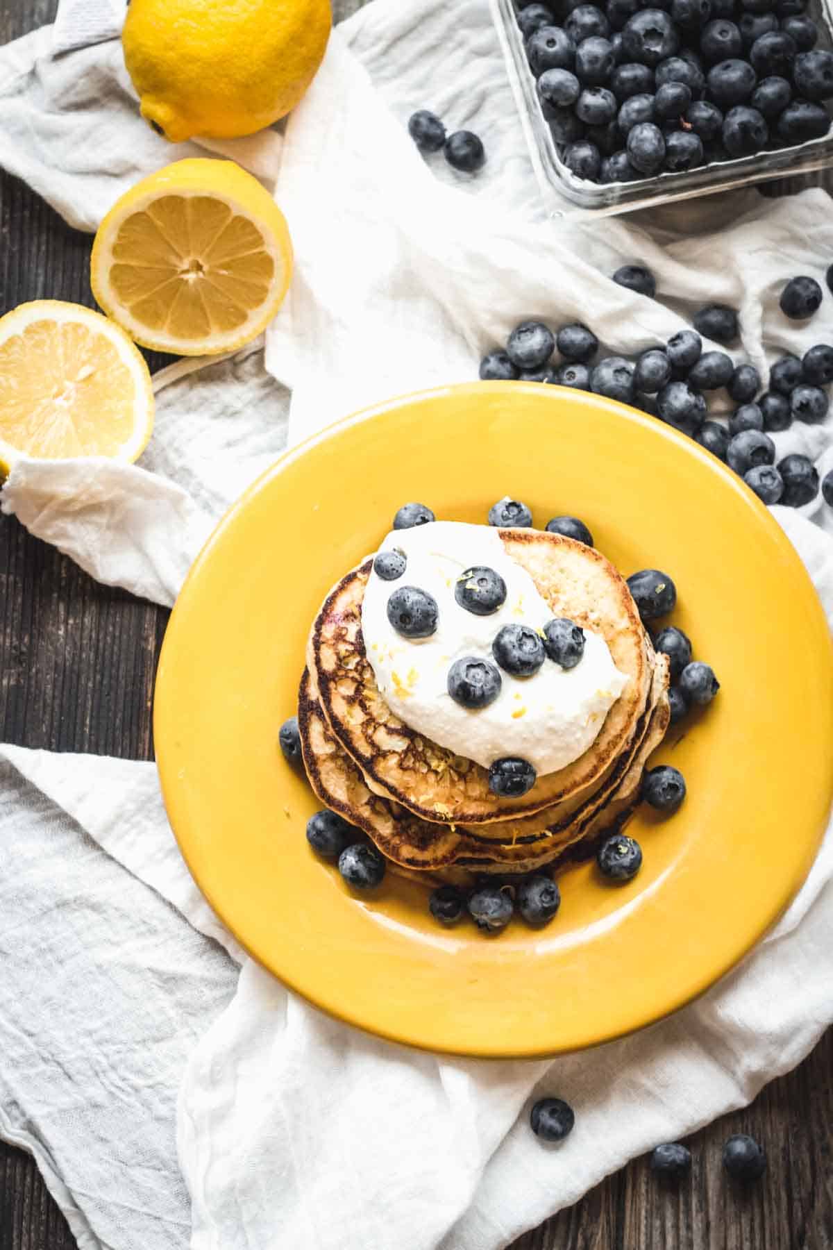 A yellow plate with pancakes, ricotta and blueberries with a lemon in the background.