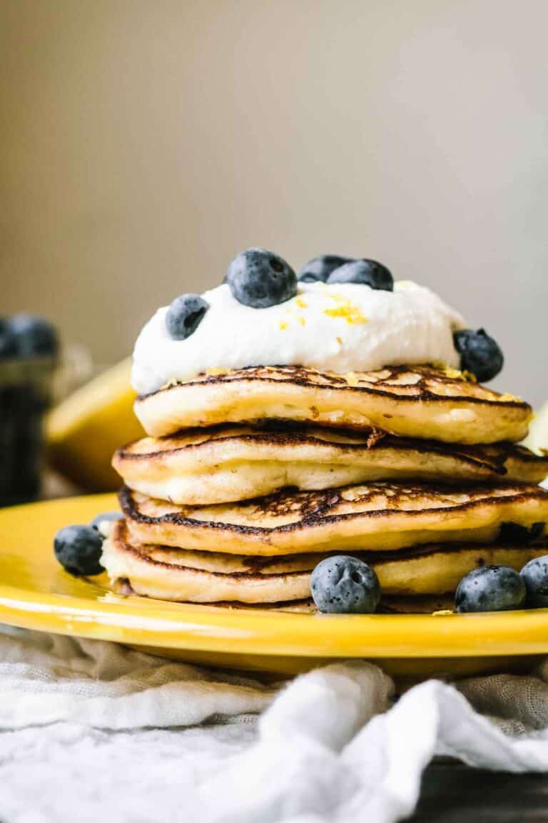 A stack of fluffy pancakes with a dollop of ricotta and fresh blueberries.