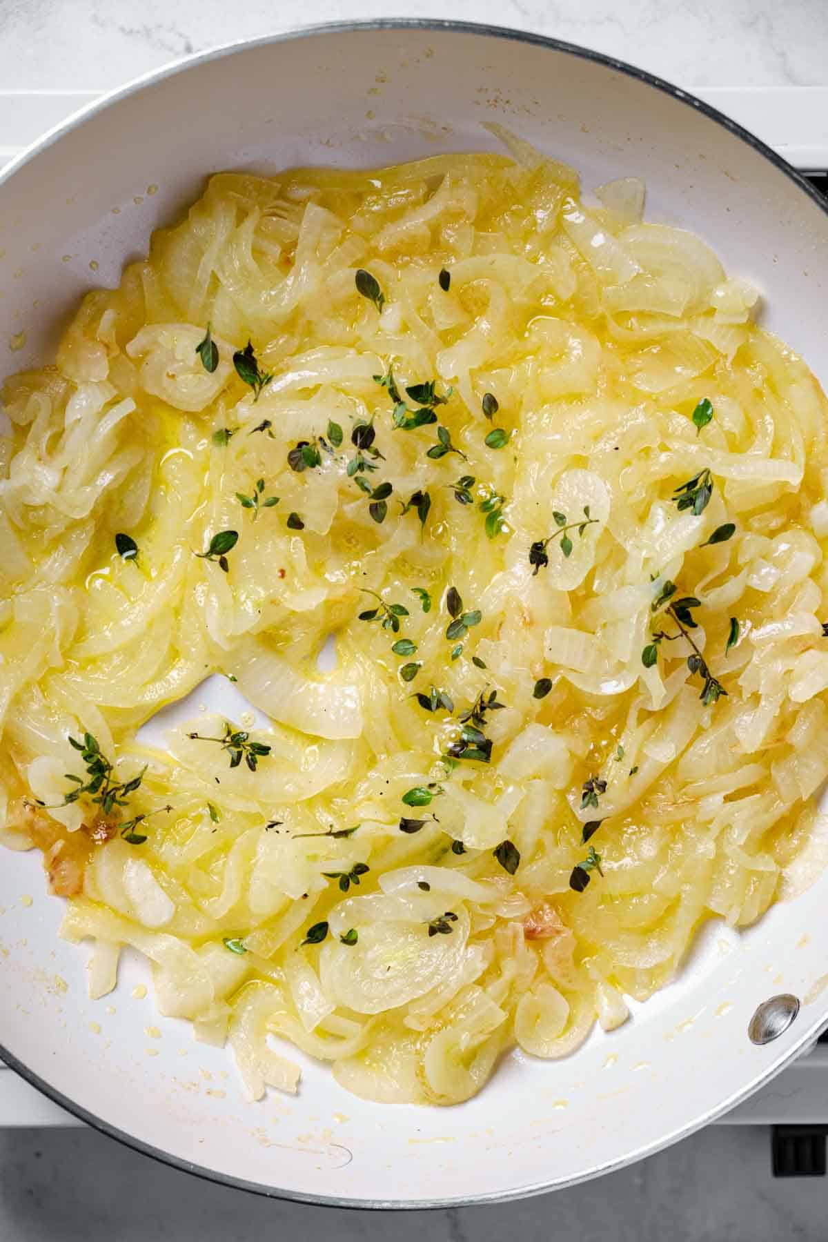 Onions cooking in a pan with fresh thyme.