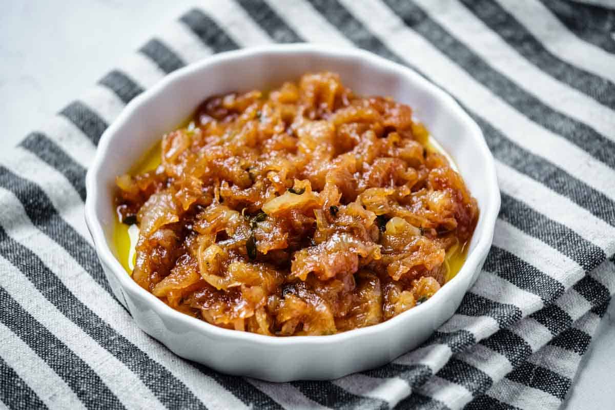 A shallow bowl of caramelized onions on a striped towel.