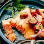 Roasted salmon on a plate with tomatoes and a bite taken out of it.