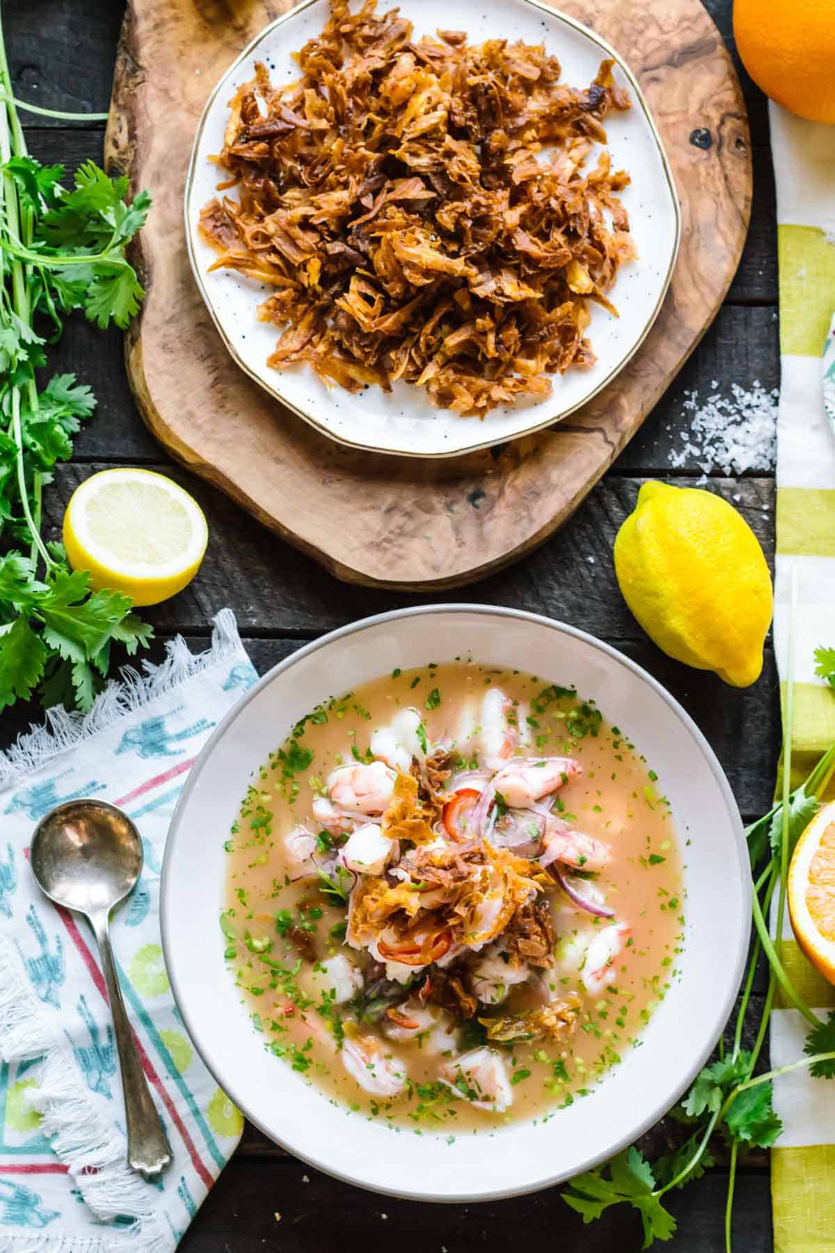 A soup bowl filled with shrimp ceviche and a plate of fried plantains.